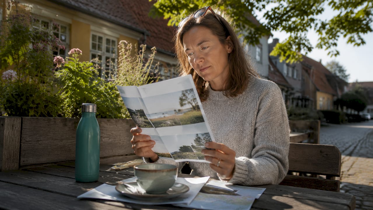 Eine Frau sitzt in einem Café und vertieft sich in eine Broschüre über nachhaltige Urlaubserlebnisse.