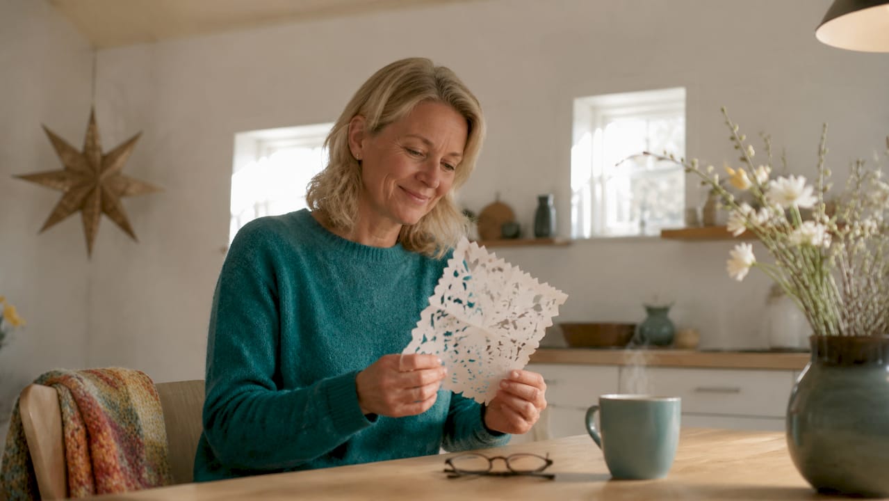 A Danish woman is sitting inside reading an old-fashioned letter on paper.