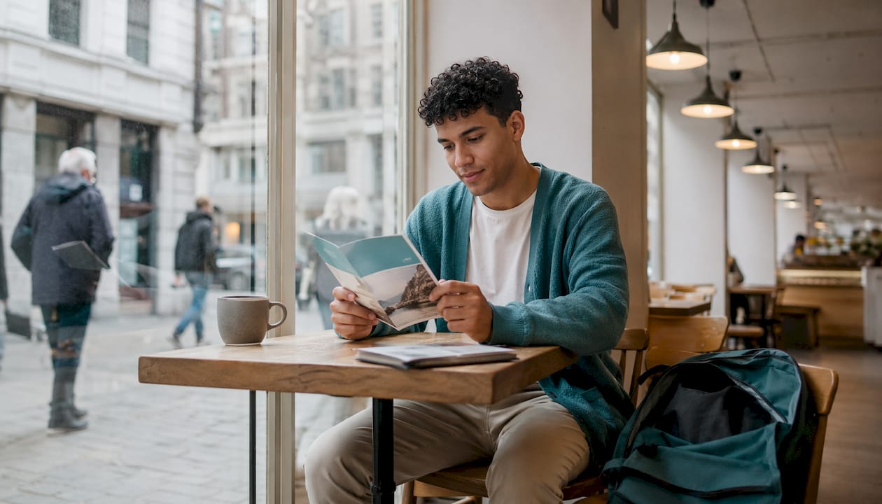 A young man is sitting and carefully reading a brochure about health insurance.