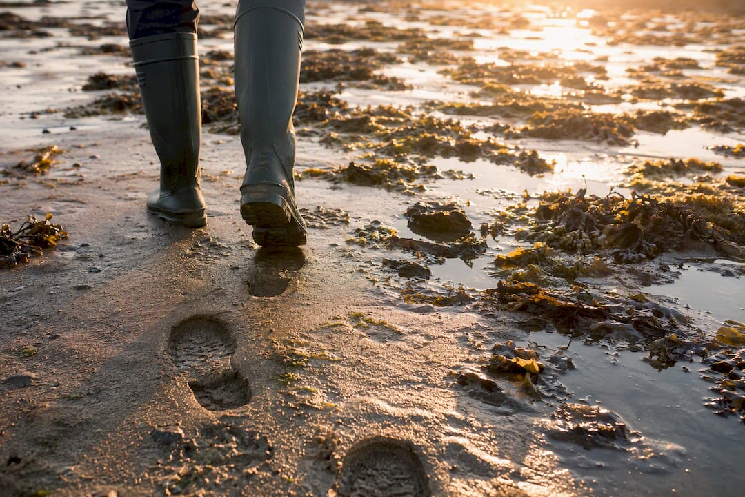 Gummistiefel gehen am nassen Sandstrand
